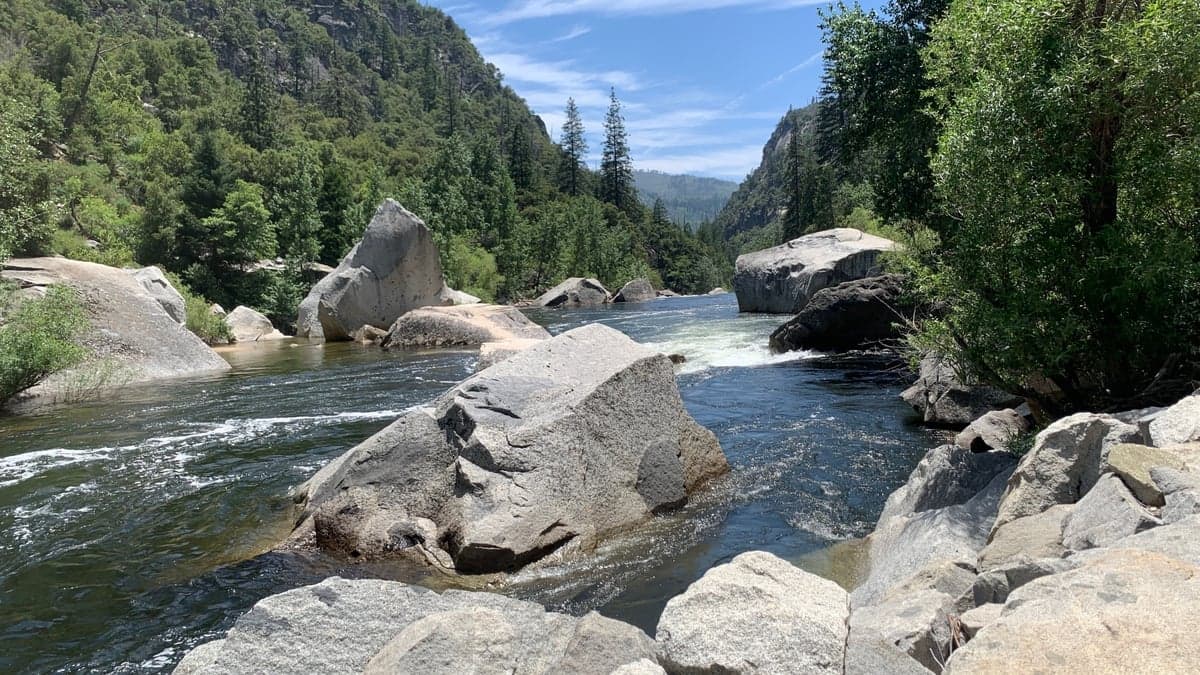 Clear river running between large granite boulders and conifers in a steep-walled canyon