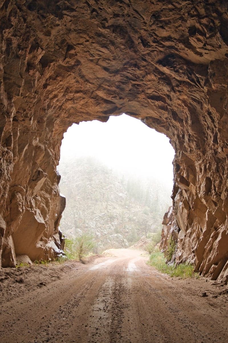 An unlit rock tunnel over a dirt road running through a canyon